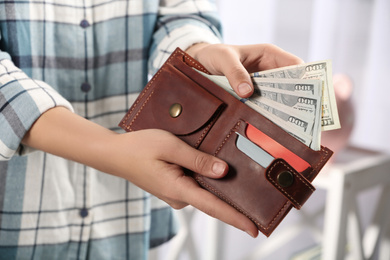 Woman putting money into wallet on blurred background, closeup