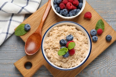 Tasty oatmeal porridge with berries on grey wooden table, flat lay