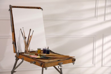 Easel with blank canvas, palette and brushes in art studio. Space for text