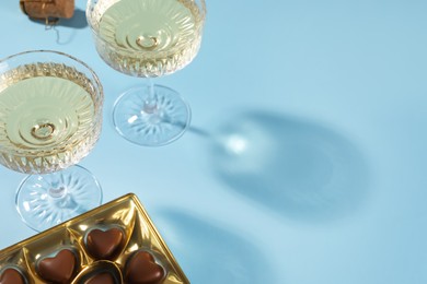 Photo of Glasses of expensive white wine and heart shaped chocolate candies on light blue background. Space for text