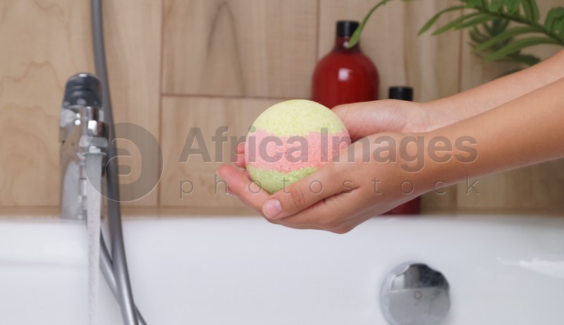 Photo of Woman holding bath bomb above tub indoors, closeup