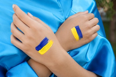 Woman with drawings of Ukrainian flag on hands outdoors, closeup