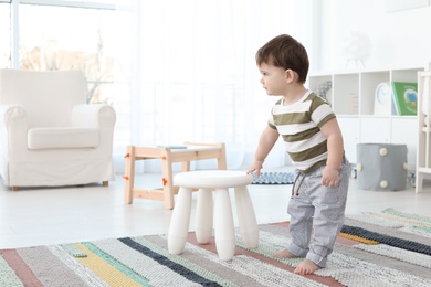 Photo of Cute baby holding on to stool at home.  Learning to walk