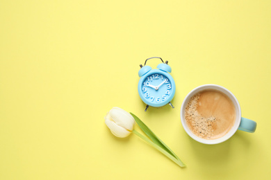 White tulip, alarm clock and coffee on yellow background, flat lay with space for text. Good morning