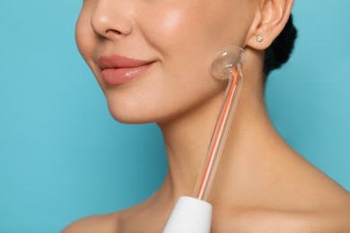 Woman using high frequency darsonval device on light blue background, closeup