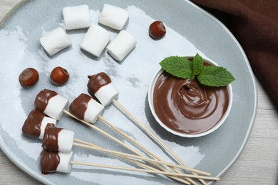 Tasty marshmallows dipped into chocolate on white wooden table, top view
