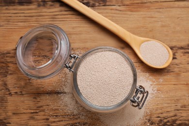 Photo of Glass jar and spoon with active dry yeast on wooden table, flat lay