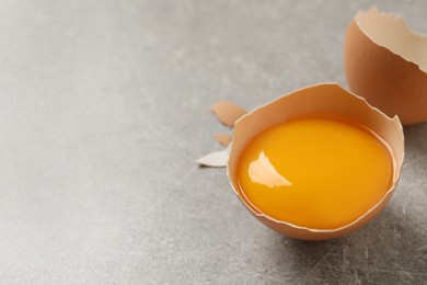 Photo of Raw yolk in broken chicken eggshell on light grey table, closeup. Space for text