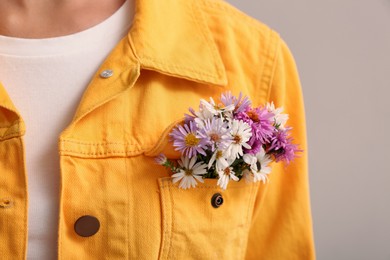 Woman with beautiful tender flowers in jacket's pocket on light background, closeup