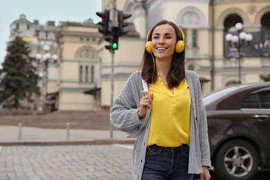 Photo of Young woman with headphones crossing street at traffic lights
