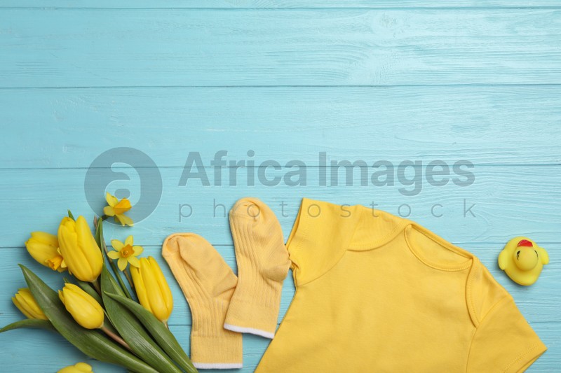 Photo of Flat lay composition with child's clothes and flowers on light blue wooden table. Space for text