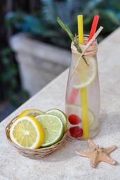 Refreshing tasty lemonade served in glass bottle and citrus fruits on beige table