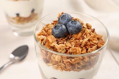 Glass of tasty yogurt with muesli and blueberries served on white table, closeup