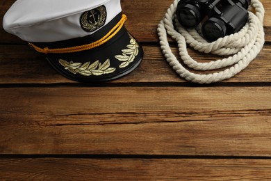 Peaked cap and rope with binoculars on wooden background, space for text