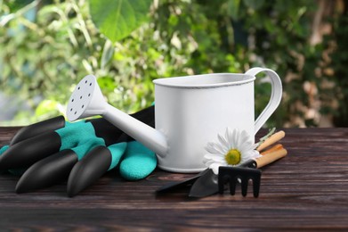 Photo of Watering can, flower and gardening tools on wooden table outdoors