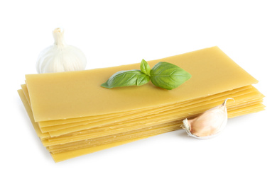 Uncooked lasagna sheets, garlic and basil on white background