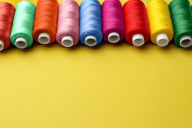 Set of colorful sewing threads on yellow background. Space for text