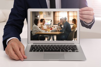 Businessman attending online video conference via modern laptop at table in office, closeup