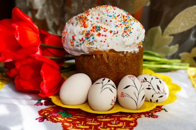 Eggs with floral ornaments and kulich for Easter near bouquet of red tulips on table