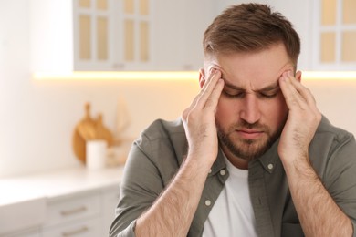 Man suffering from migraine at home, space for text
