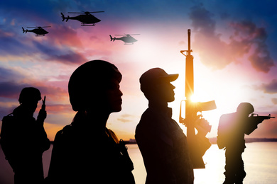 Silhouettes of soldiers in uniform with assault rifles and military helicopters patrolling outdoors