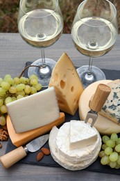 Different types of delicious cheeses, snacks and wine on wooden table outdoors