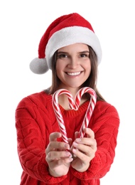 Pretty woman in Santa hat and sweater making heart with candy canes on white background