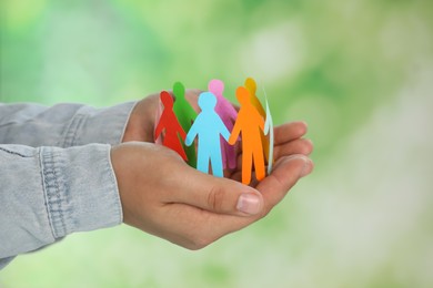 Photo of Man holding paper human figures on blurred background, closeup. Diversity and Inclusion concept
