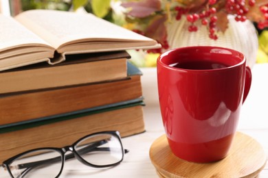 Cup with hot drink, stack of books and glasses on white wooden table. Autumn atmosphere