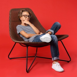 Cute little boy sitting in chair on red background