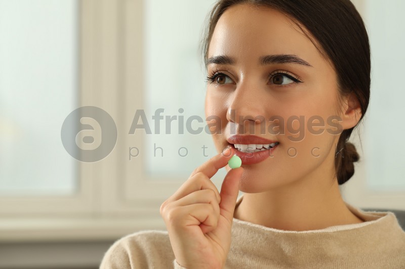 Young woman taking dietary supplement pill indoors, space for text