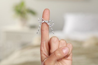 Photo of Woman showing index finger with tied bow as reminder on blurred background, closeup