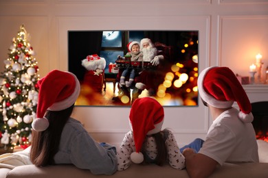 Image of Family watching TV movie in room decorated for Christmas, back view