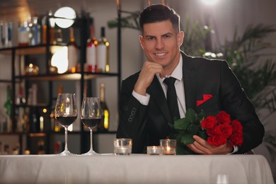 Happy man with roses waiting for his girlfriend in restaurant on Valentine's day