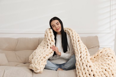 Photo of Young woman with chunky knit blanket on sofa at home