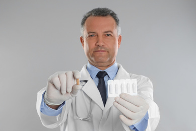 Doctor holding suppositories for hemorrhoid treatment on light grey background