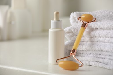 Natural face roller, towels and serum on white table, closeup. Space for text