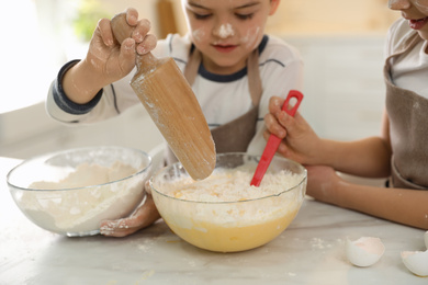 Cute little children cooking dough together in kitchen, closeup