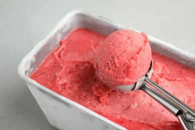 Container with delicious pink ice cream and scoop on grey table, closeup