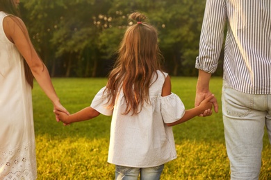 Photo of Little girl and her parents holding hands in park. Happy family
