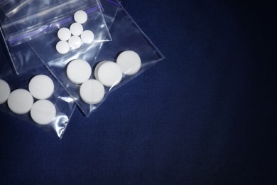 Ecstasy pills in plastic bags on color background, top view. Space for text
