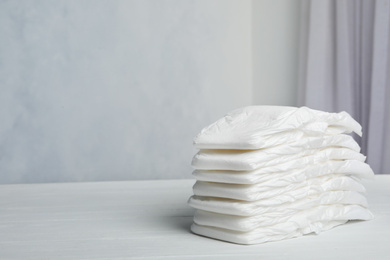 Stack of baby diapers on white wooden table against grey background. Space for text
