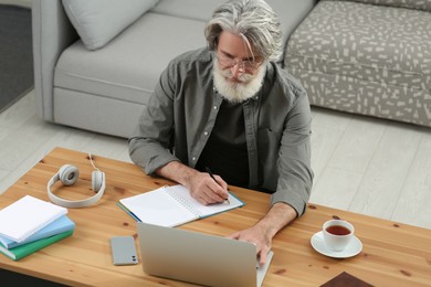 Middle aged man with laptop and notebook learning at table indoors