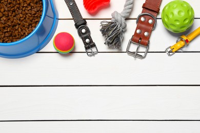 Flat lay composition with dog collars, toys and food on white wooden table. Space for text