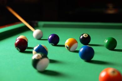Photo of Many colorful billiard balls and cue on green table indoors
