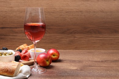 Glass of delicious rose wine and snacks on wooden table. Space for text