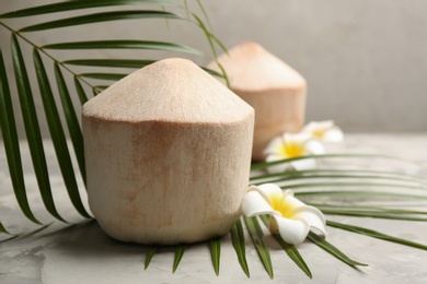 Young peeled coconuts with palm leaf and beautiful flower on grey table
