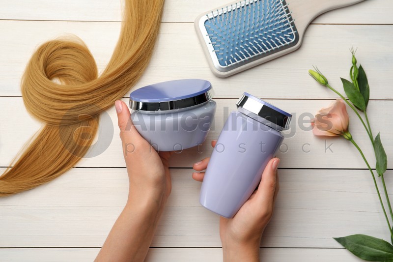 Woman holding hair care cosmetic products at white wooden table, top view