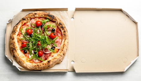 Tasty pizza with meat and arugula in cardboard box on white table, top view