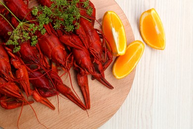 Delicious red boiled crayfish and orange on white wooden table, top view